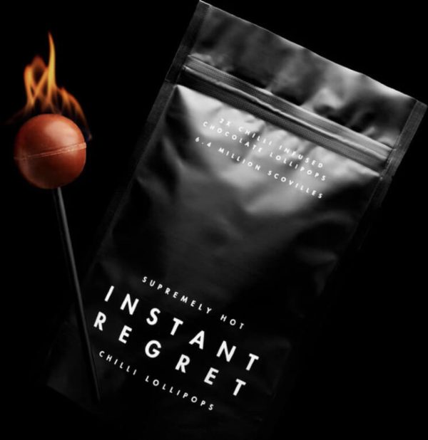 A close-up image of a red lollipop with a warning sign on its wrapper that reads "Instant Regret: World's Hottest Lollipop